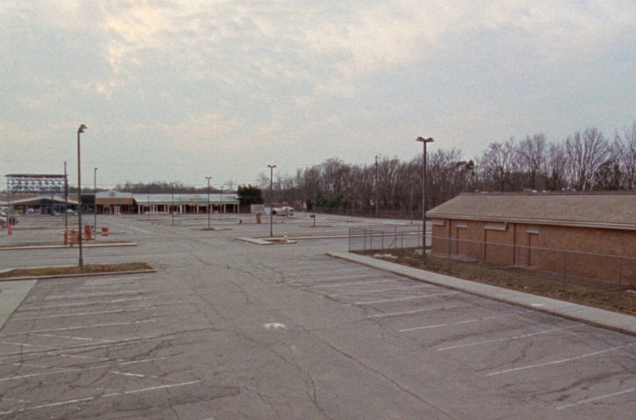 An empty asphalt parking lot on an overcast morning, faded white parking stripes and tall light poles, no cars and no people.