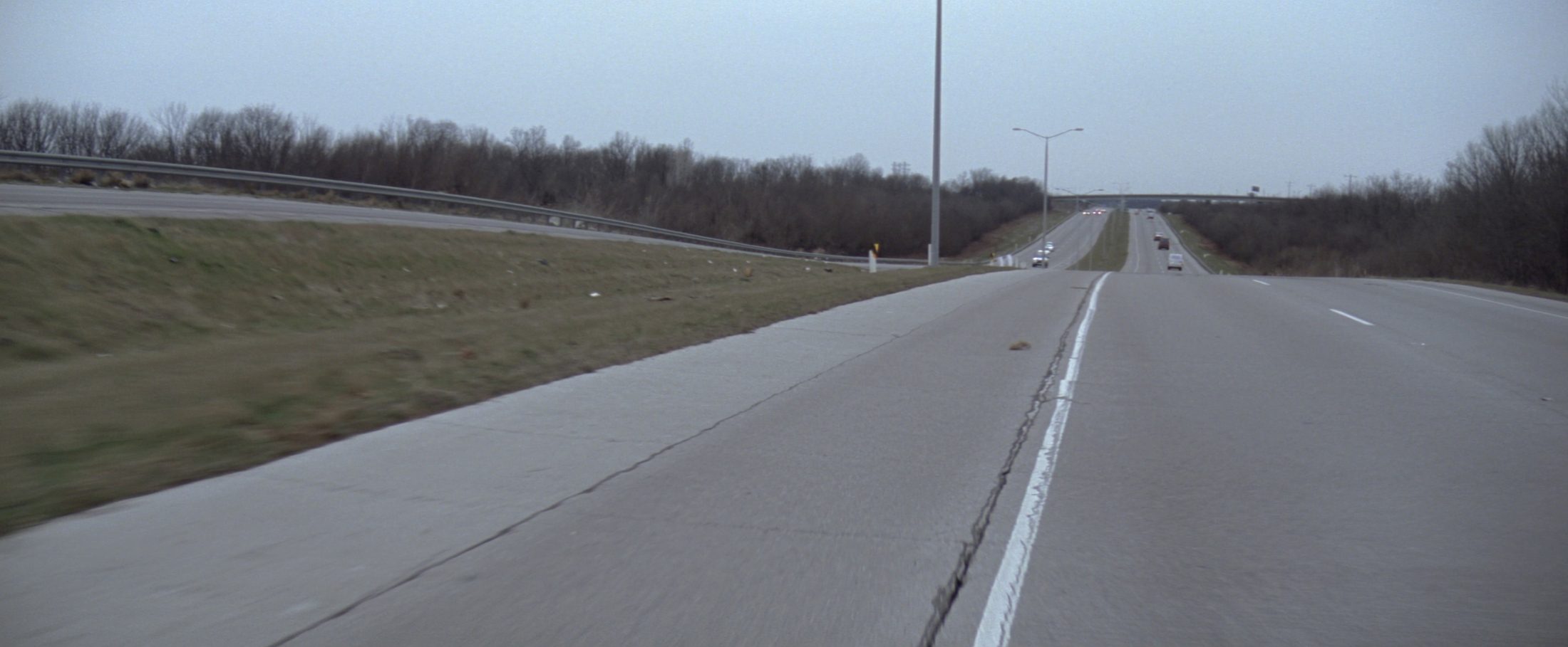 An interstate on-ramp acceleration lane merging into a Missouri highway, photographed from the grass shoulder under flat overcast light.